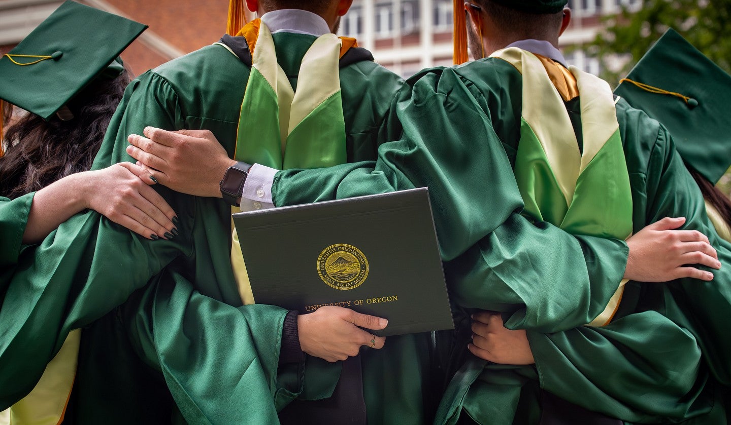 Three graduating master's students stand with arms interlocked behind each other's backs.