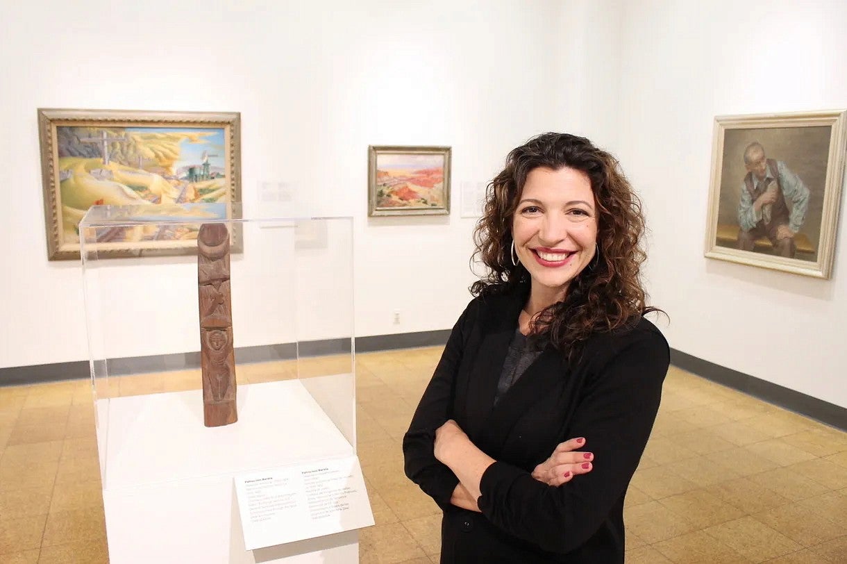 Olivia Miller has curly brown hair and is standing with her arms crossed in a museum.