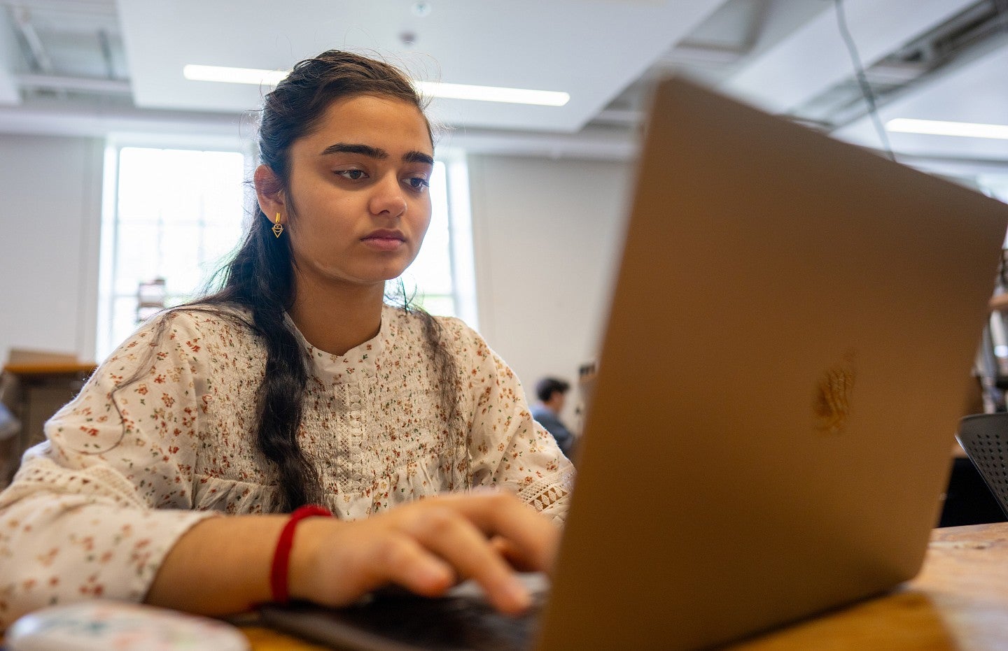 A student with long dark hair and a serious expression types on a laptop.