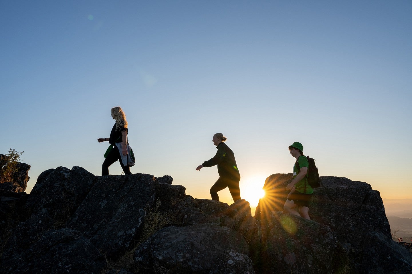 Three students climbing Spencer's Butte with the sun behind them.