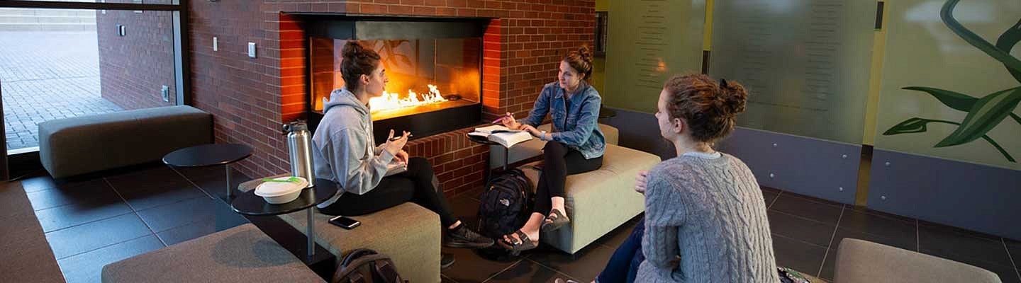Three females sitting around the fireplace in the HEDCO building