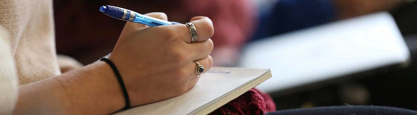 Hand holding a pen while writing in a notebook Hand holding a pen while writing in a notebook