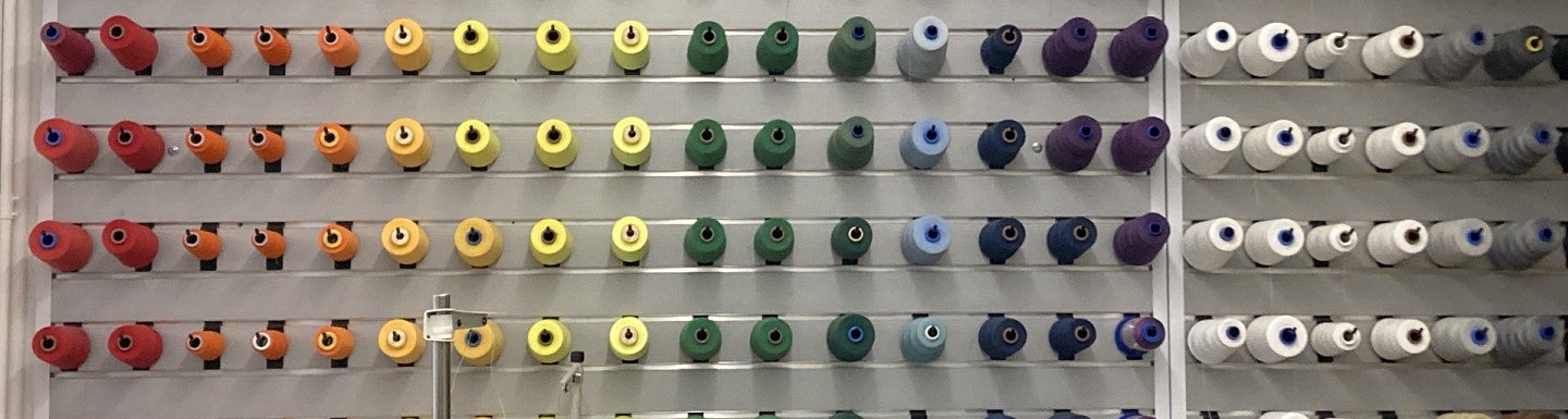 Spools of thread sorted by color on a wall. The spools are organized in the color pattern of a rainbow