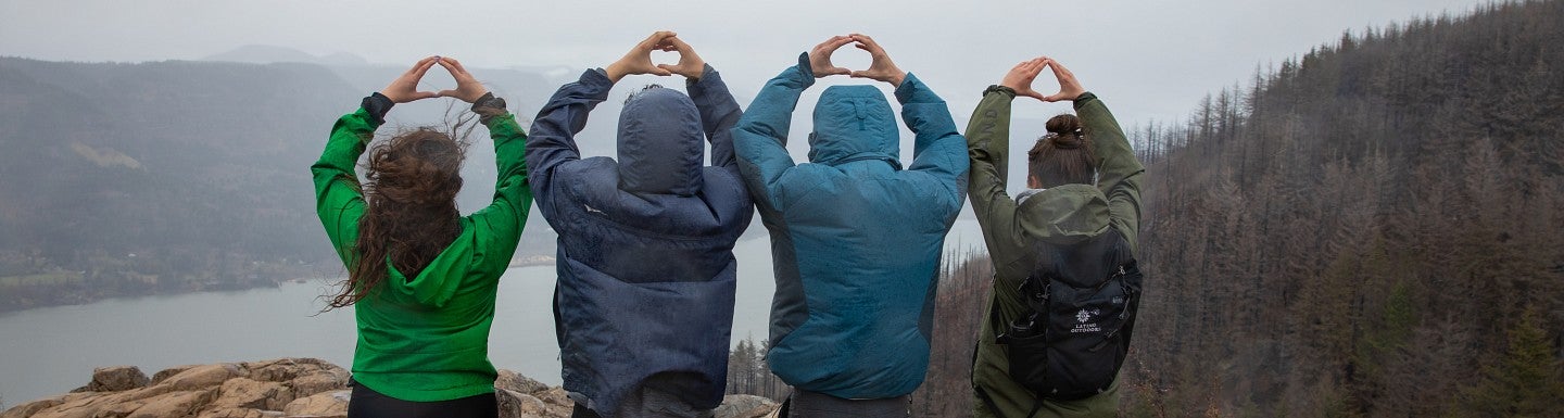 Four students wearing jackets, as seen from behind. They have their hands over their heads and are making the letter "O" with their fingers.
