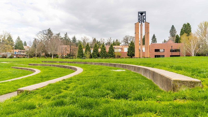 Brick buildings behinds a grassy lawn with concrete , arc shaped seating resembling an amphitheater.