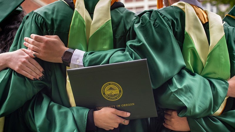 Three graduating master's students stand with arms interlocked behind each other's backs.