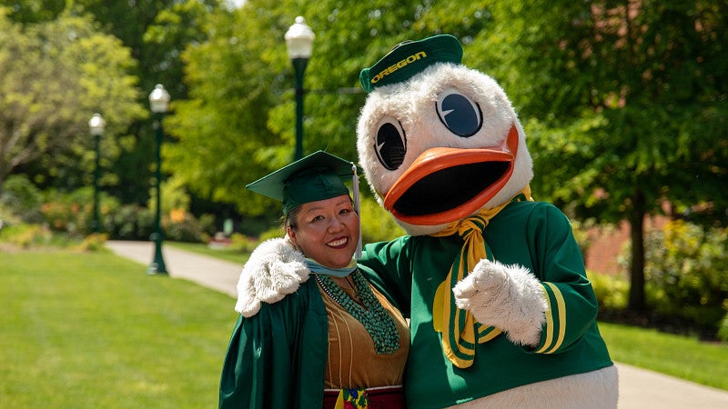 Uo duck mascot with a graduate student at comencement