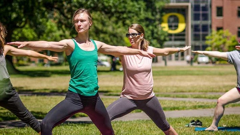 People performing yoga on the quad in front of the Lillis Business Complex