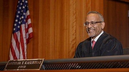 Mustafa T. Kasubhai, a Muslim American judge, smiles behind his bench.