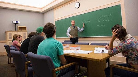 A professor teaching on a chalkboard in a small class