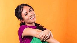 Carmelli Hess smiles at the camera in front of a bright orange background.