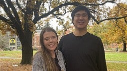 Emily Arnesen and Kyutaro Matsuzawa stand together under autumn foliage.