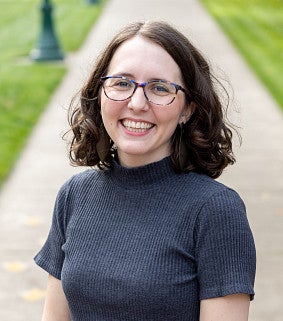 Audrey has short brown curly hair and glasses.