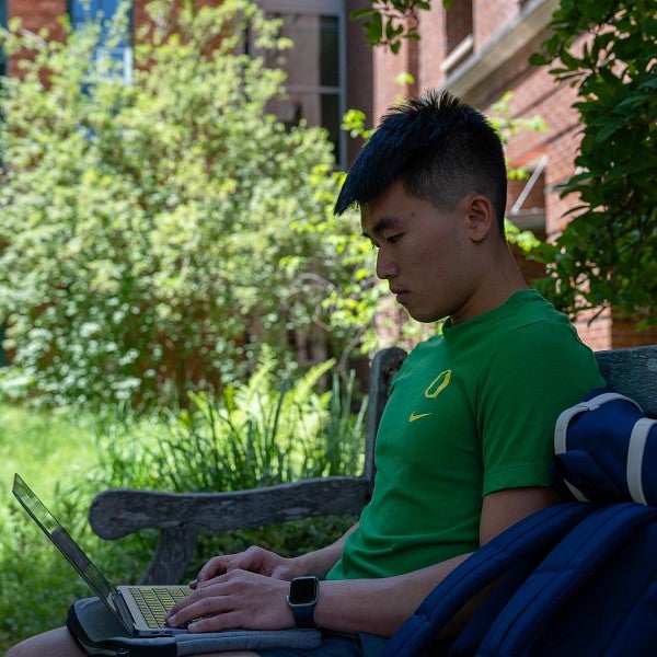 international student looks at laptop while sitting on bench