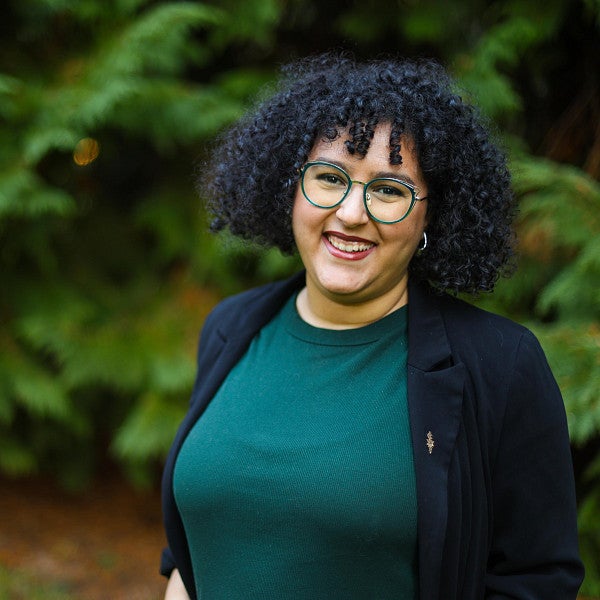 Nahla Bendefaa has dark curly hair and is wearing green framed glasses and red lipstick.