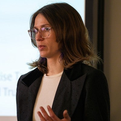 Graduate student with short brown hair and glasses giving a presentation.