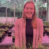 Smiling person in a greenhouse filled with plants.