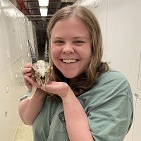 Smiling person holding small mammal skull.