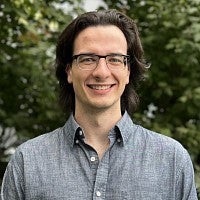 Smiling man with dark hair and glasses.