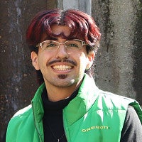 Isaac Membreno has short red hair and is wearing glasses and a green Oregon vest.