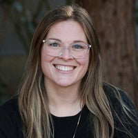 Kaisa Lightfoot has long medium brown hair and is wearing glasses and a black shirt.